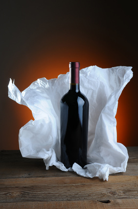 Red Wine Bottle with tissue paper wrapping on wood surface and light to dark warm background.