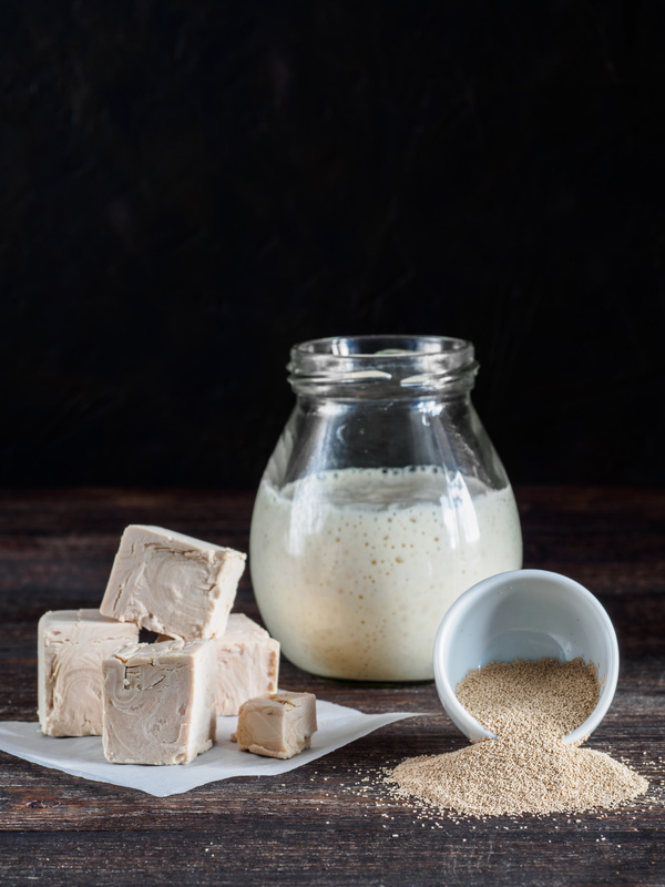 Different types yeast. Fresh pressed yeast, dry instant yeast and active wheat sourdough starter (wild yeast) on wooden table. Low key. Selective focus. Copy space. Vertical.