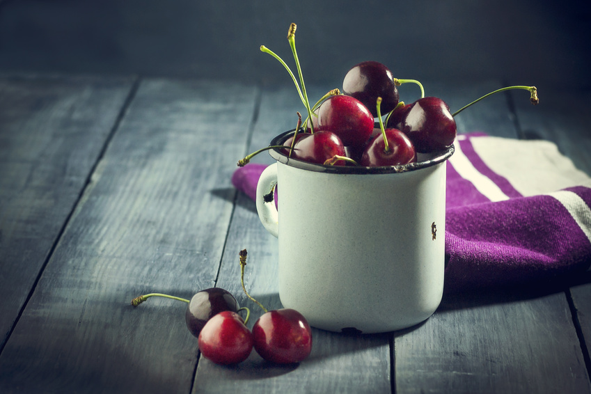 Ripe cherries in an iron mug on a dark blue wooden background. With copy space.